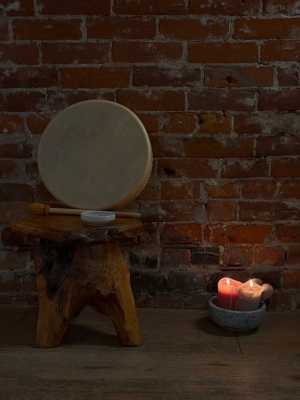 A frame drum and candles against a brick wall